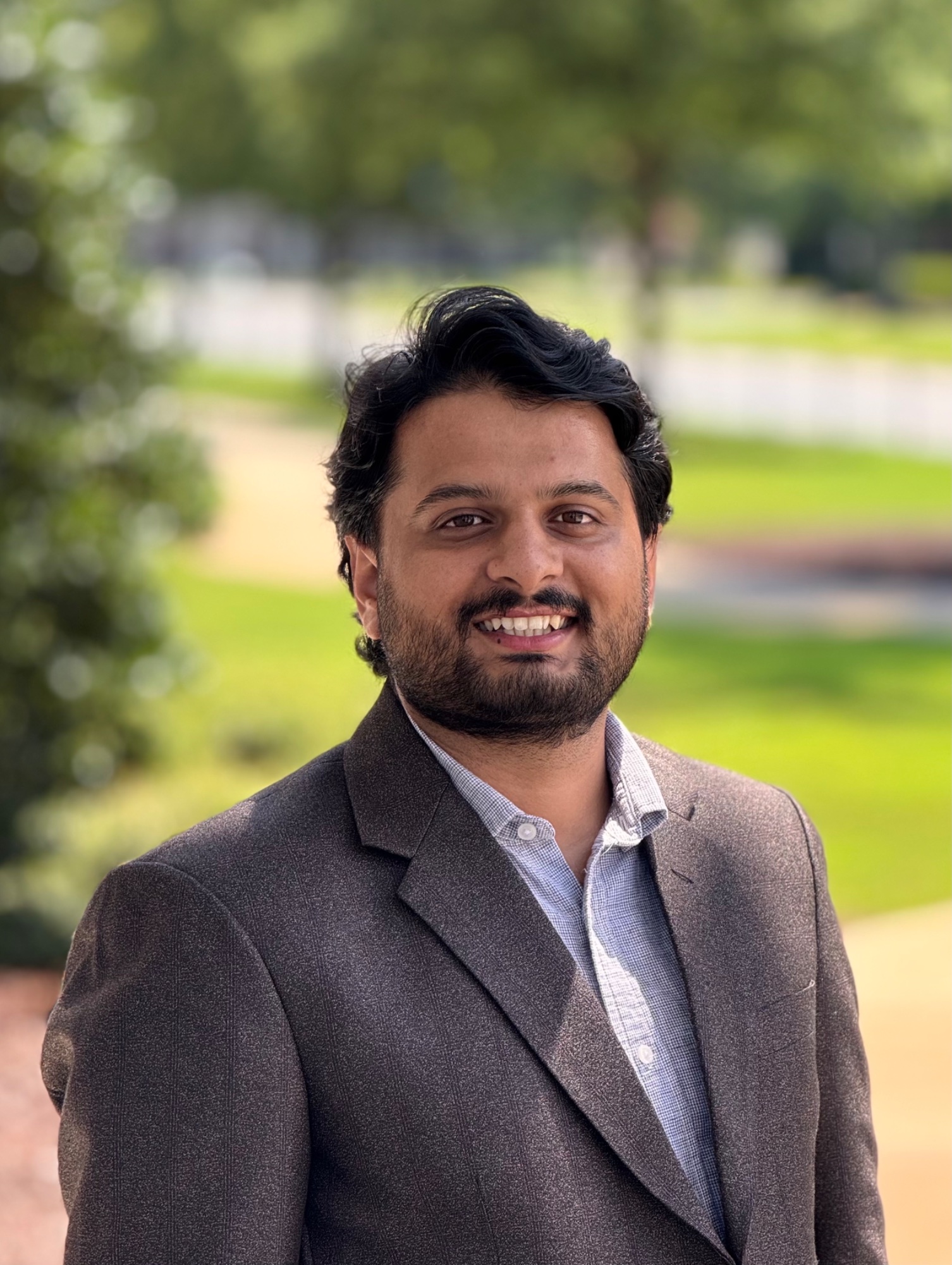 Supath Dhital — smiling headshot outdoors in a grey blazer